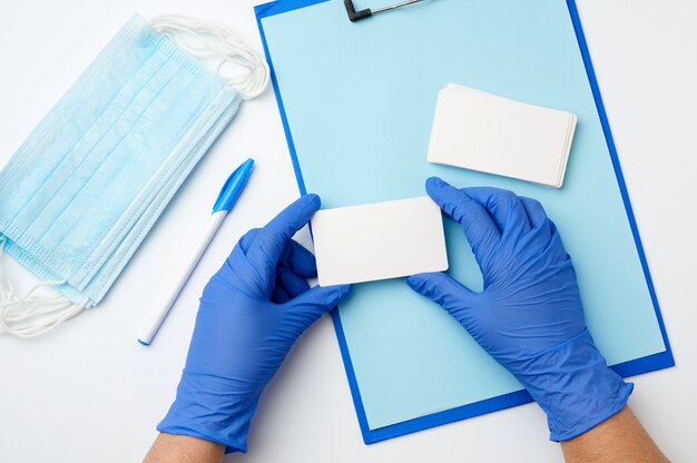 Twee handen in blauwe medische handschoenen houden rechthoekige witte blanco visitekaartjes