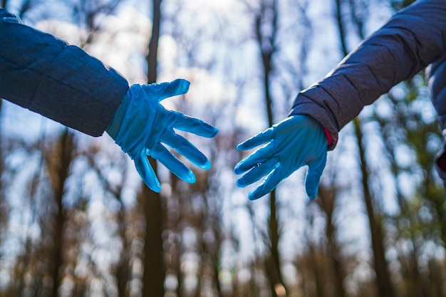 Twee handen in latexhandschoenen die elkaar proberen aan te raken. bomen achtergrond. mensen in park. selectieve aandacht.