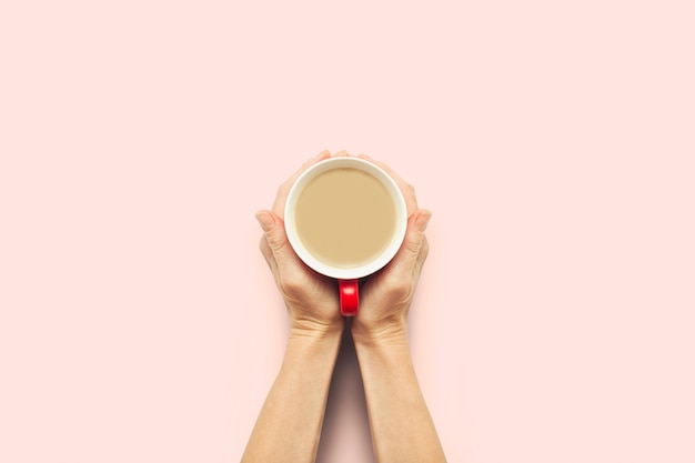 Twee handen met een kopje warme koffie op een roze achtergrond. Ontbijtconcept met koffie of thee. Goedemorgen, nacht, slapeloosheid. Plat lag, bovenaanzicht