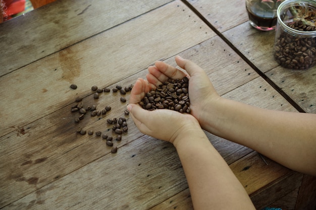 Twee handen met koffiebonen en wat zaad viel op een houten tafel.