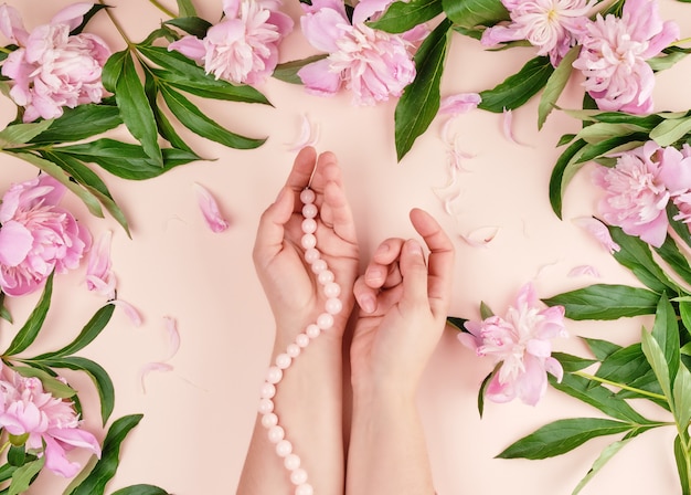 Twee handen van een jong meisje met een vlotte huid en een boeket van roze pioenrozen op perzik bloemen