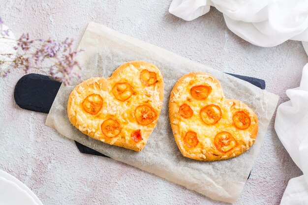 Twee hartvormige kant-en-klare pizza's op papier op gedekte tafel voor valentijnsdagviering. Detailopname. Bovenaanzicht