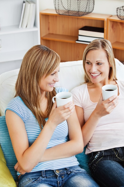 Twee heldere vrouwen die koffie samen op een bank drinken