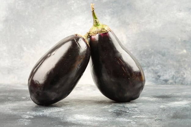 Twee hele auberginegroente die op een marmeren tafel wordt geplaatst.