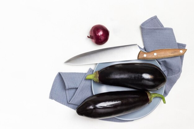 Twee hele aubergines op een grijs bord op een grijze servet keukenmes op tafel