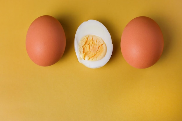 Twee hele bruine eieren en een gekookt ei met dooier in tweeën gesneden op een geïsoleerde lichtgele achtergrond