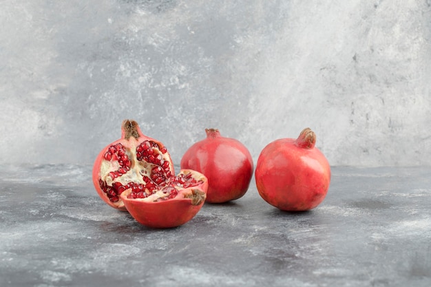 Twee hele granaatappels en gesneden granaatappels op marmeren achtergrond.