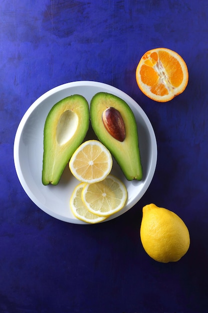 Twee helften van een rijpe avocado met zaad op een witte plaat Close-up groen gezond fruit met citrusvruchten op een blauwe achtergrond