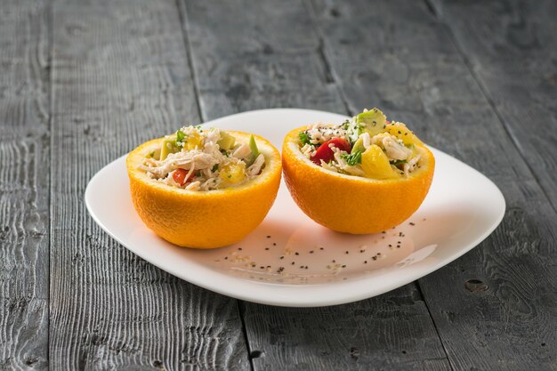 Twee helften van sinaasappel met avocado salade en kip op een witte plaat op een houten tafel. Dieetvoeding van tropisch fruit en kip.