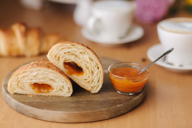 Twee helften van vers ontblootte croissant op houten bord met heerlijke zelfgemaakte abrikozenjam.