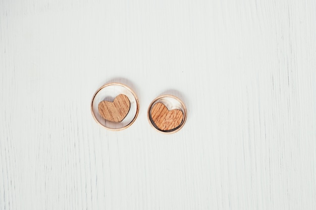 Twee houten harten in de gouden ringen van het paarhuwelijk op witte achtergrond. Overhead schot.