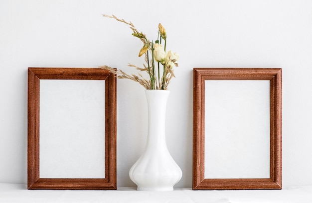 Twee houten lijsten met een wit inzetstuk aan de binnenkant en witte gedroogde bloemen in een witte vaas Fotolijst op een witte muurachtergrond