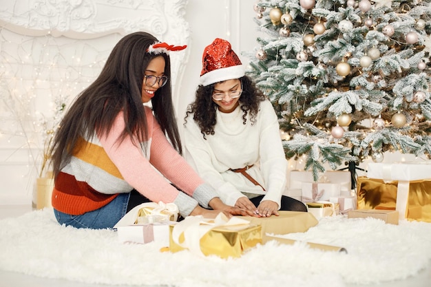 Twee Indiase meisjes met een bril verpakken een cadeau in een papier bij de kerstboom