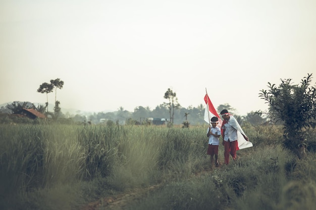 Twee Indonesische scholieren die vlag in het padieveld houden. Trotse basisschoolleerling viert in