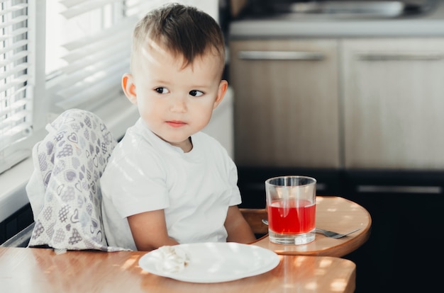 Twee jaar jongen die sap drinkt uit een glazen beker in de keuken