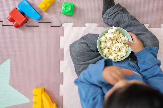 Twee jaar oude Mexicaanse babyjongen die popcorn eet op rommelige kamer