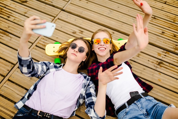 Twee jong meisje in hipster outfit selfie maken terwijl liggend met op houten pier.