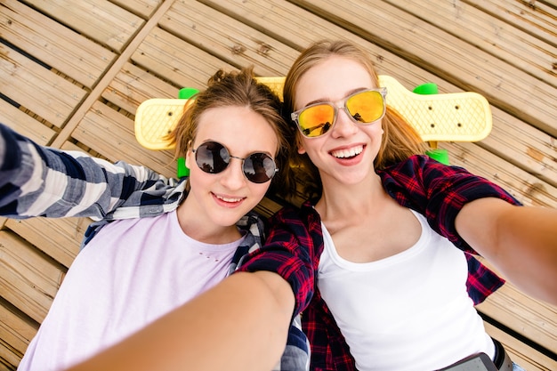 Twee jong meisje in hipster outfit selfie maken terwijl liggend met op houten pier.