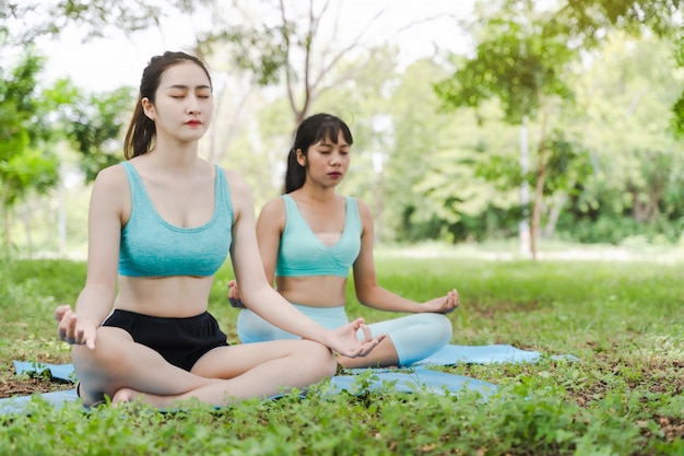 Foto twee jonge aantrekkelijke atleten aziatische vrouw het praktizeren yoga in de parkaard openlucht op groen gras in de ochtend