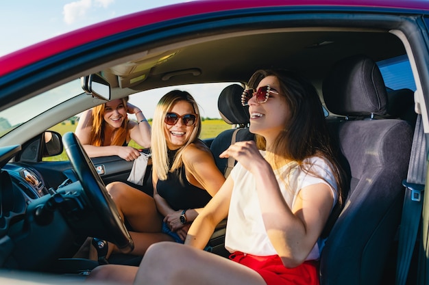 Twee jonge aantrekkelijke meisjes zitten in de autosalon en kletsen met de derde achter het raam, vrouwelijke positieve reisavonturen.