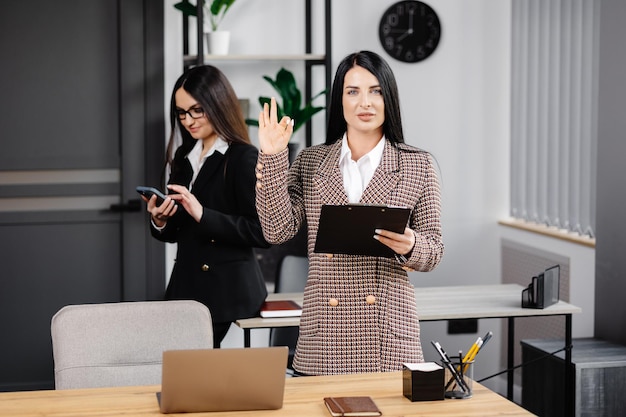 Twee jonge, aantrekkelijke vrouwen werken op kantoor Een vrouw is aan het telefoneren en haar collega maakt aantekeningen in een notitieboekje