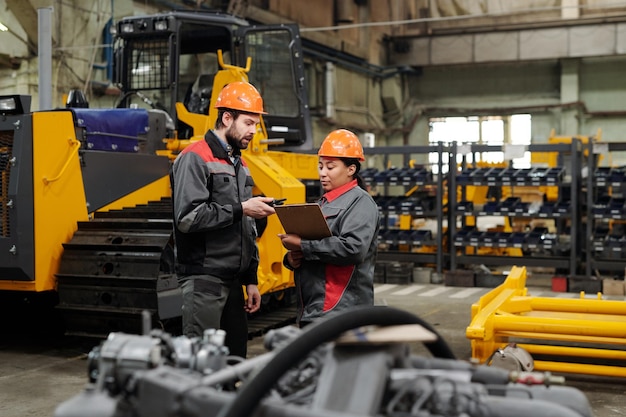 Twee jonge arbeiders van industriële fabrieken in werkkleding bespreken gegevens in document