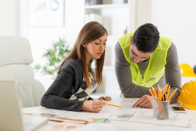 Twee jonge architecten die de bouwplannen op kantoor controleren.