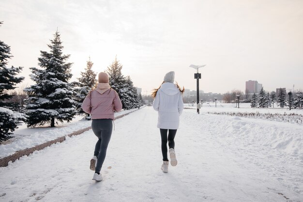 Twee jonge atletische meisjes lopen in het park op een zonnige winterdag. Een gezonde manier van leven.
