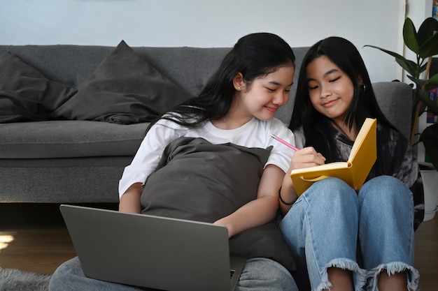 Twee jonge Aziatische meisjes zitten in de woonkamer en maken samen huiswerk