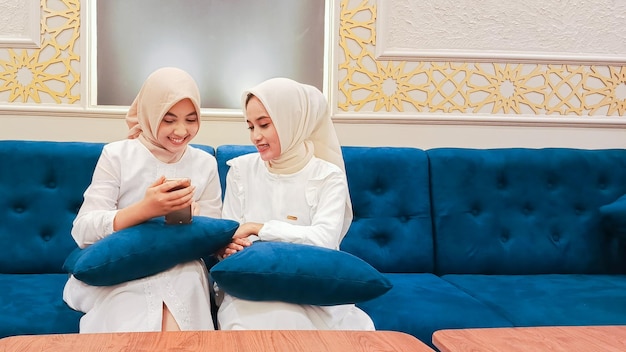 twee jonge Aziatische vrouwen met oprechte gelukkige glimlachjes praten over iets voor een smartphone met een achtergrond