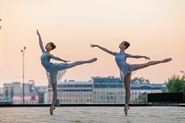 Twee jonge ballerina's dansen in pointe-schoenen in de stad tegen de achtergrond van de avondrood