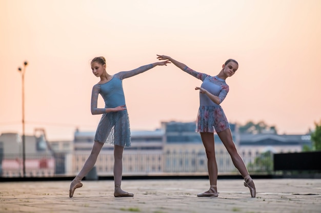 Twee jonge ballerina's dansen in pointe-schoenen in de stad tegen de achtergrond van de avondrood