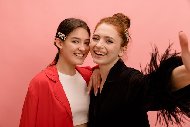 Twee jonge blanke brunette en roodharige in rode zwarte shirts glimlachen naar de camera en nemen selfie op roze achtergrond Lifestyle verschillende emoties vrije tijd concept