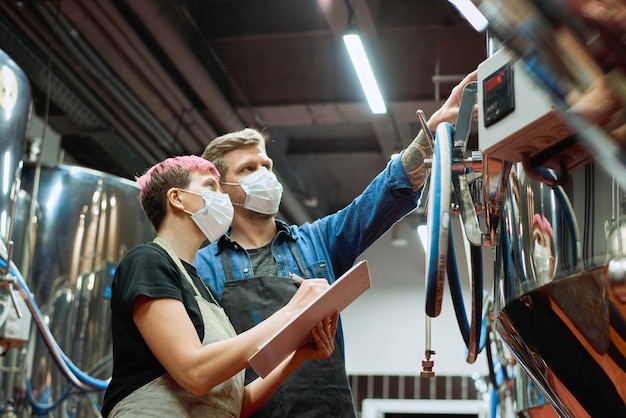 Twee jonge brouwers van een hedendaagse bierproductiefabriek die naar het bedieningspaneel kijken terwijl de man naar gegevens wijst tijdens het werk in de verwerkingsfabriek