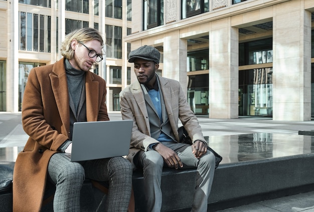 Twee jonge collega's die laptop gebruiken en online discussiëren, werken buitenshuis samen