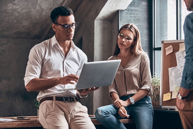 Twee jonge collega's in slimme vrijetijdskleding die zaken bespreken en laptop gebruiken