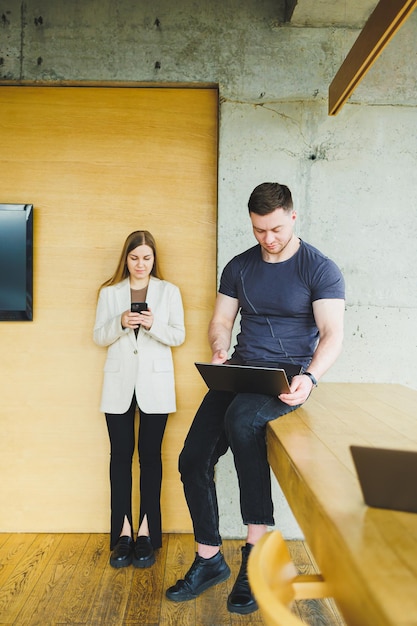 Twee jonge collega's man en vrouw werken samen in een moderne werkruimte Twee jonge zakenmannen lachen vrolijk terwijl ze met een laptop werken Collega's zitten samen aan tafel