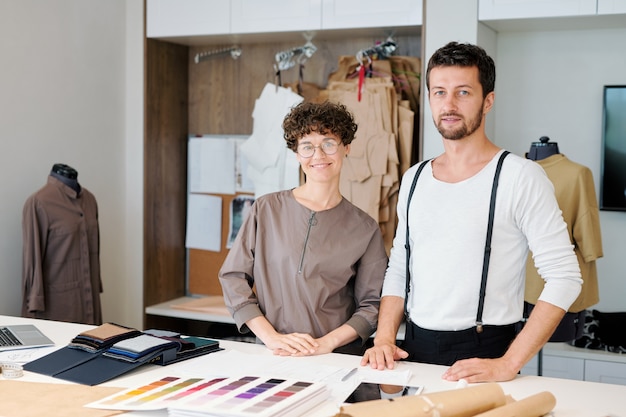 Twee jonge creatieve ontwerpers van kledingstukken die zich bij bureau bevinden terwijl zij samenwerken