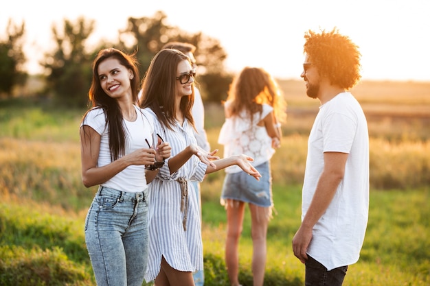 Twee jonge donkerharige vrouwen chatten met jonge krullende man buiten op een warme dag