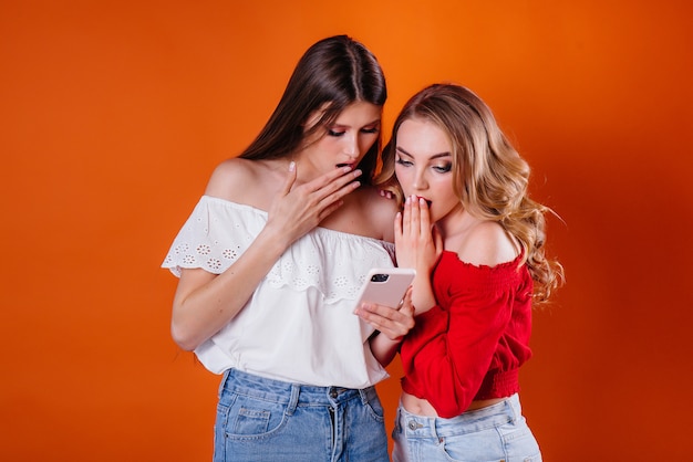 Twee jonge en mooie meisjes maken een selfie en kijken naar de telefoon in de studio op een paarse plek. Meisjes voor reclame.