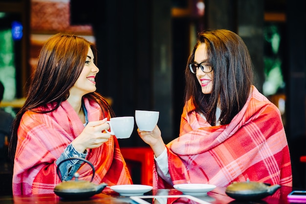 Twee jonge en mooie meisjes roddelen op het terras met een kopje koffie