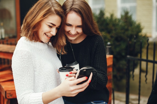 twee jonge en mooie meisjes staan ​​in een lentestad en drinken koffie