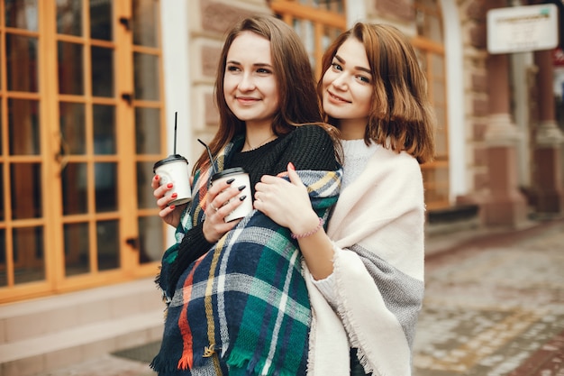 Twee jonge en mooie meisjes staan ​​in een lentestad en drinken koffie