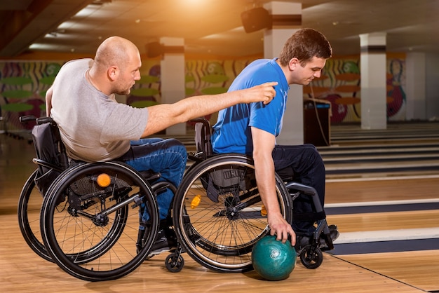 Twee jonge gehandicapte mannen in een rolstoel die bowlen in de club