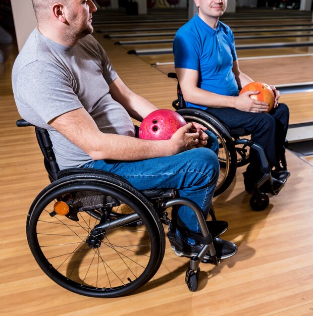 Twee jonge gehandicapte mannen in rolstoelen die bowlen in de club