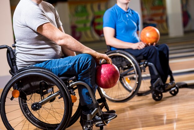 Twee jonge gehandicapte mannen in rolstoelen die bowlen in de club