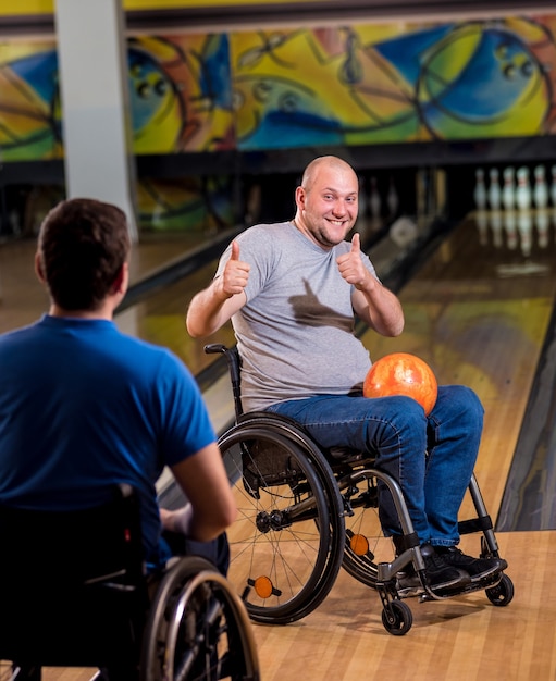 Twee jonge gehandicapte mannen in rolstoelen die bowlen in de club