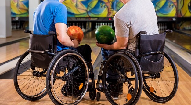 Twee jonge gehandicapte mannen in rolstoelen die bowlen in de club
