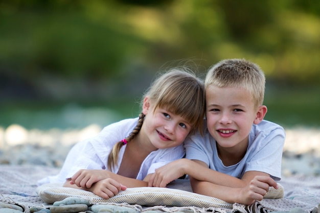 Twee jonge gelukkig schattige blonde lachende kinderen, jongen en meisje, broer en zus omarmen omarmd op kiezelstrand op wazig heldere zonnige zomerdag. Vriendschap en perfect vakantieconcept.