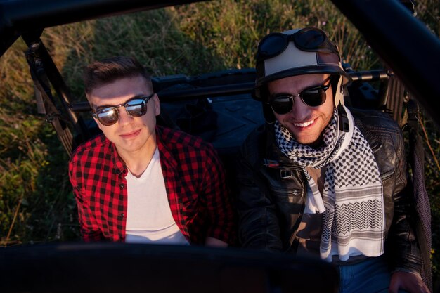 twee jonge gelukkige opgewonden mannen genieten van een mooie zonnige dag terwijl ze een off-road buggy auto rijden op de bergnatuur